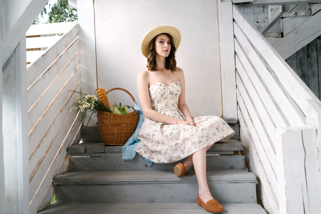THE PERFECT DRESS GUIDE A woman in a floral dress and straw hat sits with a picnic basket on rustic wooden steps.